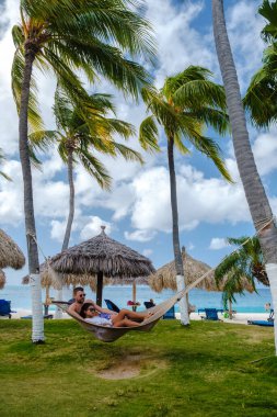 Palm Beach Aruba Karayipleri, Aruba Antilleri 'nde palmiye ağaçları olan uzun kumlu bir plajda hamakta olan birkaç erkek ve kadın..