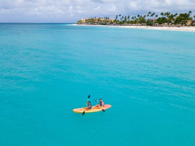 Okyanusta kayak yapan çift Aruba Karayip Denizi 'nde, orta yaşlı erkek ve kadın okyanus mavisi açık denizde kayak yapıyor beyaz plaj ve palmiye ağaçları ile Aruba