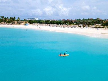 Couple Kayaking in the Ocean on Vacation Aruba Caribbean Sea, man and woman mid age kayak in ocean blue clear water with white beach and palm trees Aruba clipart