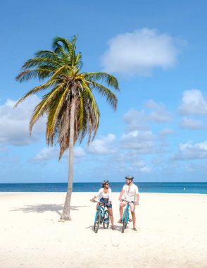 Eagle Beach Aruba, Aruba 'daki Eagle Beach sahilinde Palm Trees, birkaç adam ve Aruba sahilinde bisikletli bir kadın.