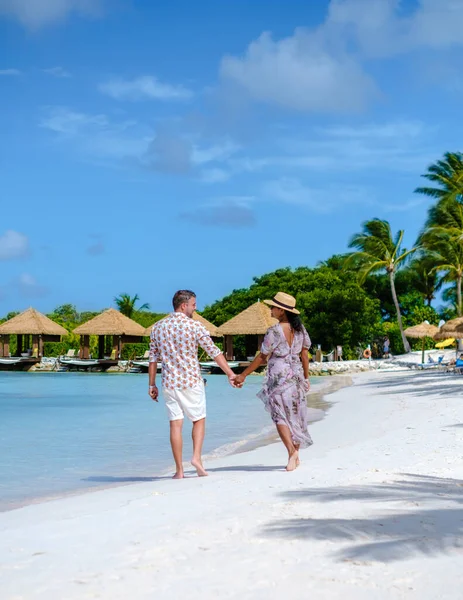 アルバ島で休暇中の男性と女性のカップルカリブ海は 豪華なリゾートでターコイズブルーの海とオーバーウォーターバンガローのヤシの木と熱帯の白いビーチを歩いています — ストック写真