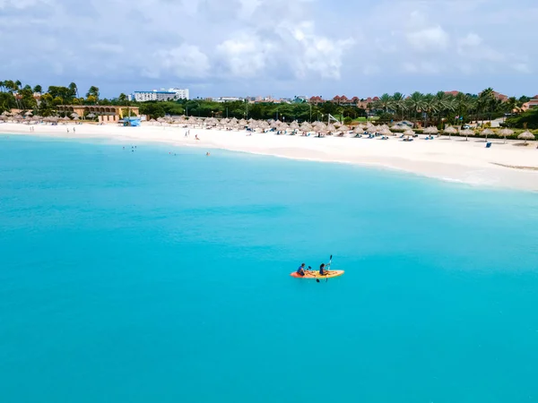 Couple Kayaking in the Ocean on Vacation Aruba Caribbean Sea, man and woman mid age kayak in ocean blue clear water with white beach and palm trees Aruba