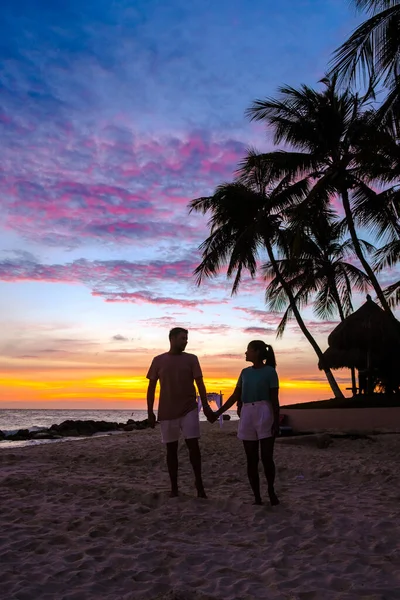 アルバ島での休暇中に夕日を見ているビーチには男性と女性のカップルがいますカリブ海 — ストック写真