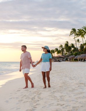 Palm Beach Aruba Karayipleri, Aruba Antilleri 'nde palmiye ağaçları ve turkuaz renkli bir okyanusu olan beyaz kumlu plajda bir çift kadın ve erkek.