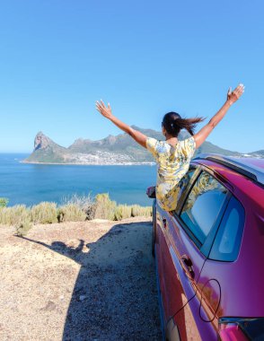 Araba penceresinin dışında elleri havada bir kadın Cape Town Güney Afrika 'da Chapmans Tepesi yolunda bir araba okyanusa bakıyor. Güney Afrika 'da bir yol gezisindeki kadınlar renal araba kullanıyorlar.