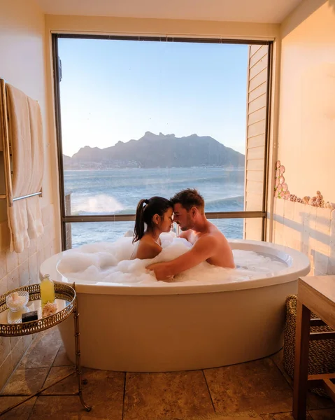 一对夫妇的男人和女人在一个浴缸里看着在开普敦的海面上度假的南非 日落时分在浴池里洗澡 在奢华的假期里穿夹克 — 图库照片