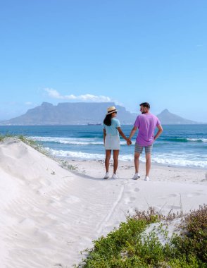 Bloubergstrand Cape Town Güney Afrika 'da güneşli bir yaz günü, Blouberg plajı, toz beyaz kum ve mavi okyanusla. Kumsalda bir çift, kumsalda takılan erkekler ve kadınlar