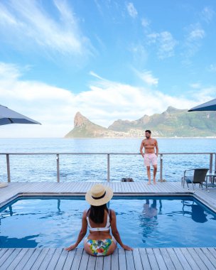 Olgun bir çift, sonsuz havuzun önünde Cape Town Güney Afrika okyanusunu seyrediyor. Gün batımında bir kadın ve erkek yüzme havuzunda.. 