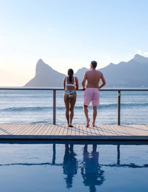 Olgun bir çift, sonsuz havuzun önünde Cape Town Güney Afrika okyanusunu seyrediyor. Gün batımında bir kadın ve erkek yüzme havuzunda.. 
