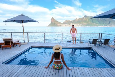 Infinity havuzunun önünde orta yaşlı bir çift gün batımında yüzme havuzunda Cape Town Güney Afrika okyanusunu seyrediyor.. 