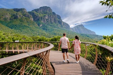 Cape Town 'daki Kirstenbosch botanik bahçesinde, Cape Town' daki Kirstenbosch Gardens 'ta yemyeşil Güney Afrika' nın üzerine inşa edilmiş bir köprü üzerinde yürüyen bir çift kadın ve erkek.