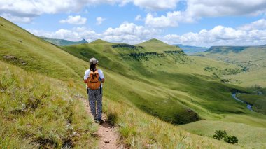 Drakensberg Dağı, Güney Afrika, Orta Drakensberg Kwazulu Natal, Güney Afrika 'da gün batımında yeşil dağların üzerinden geçen Asyalı kadınlar.