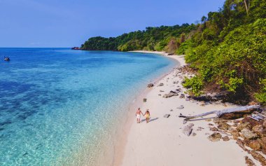 Beyaz tropikal bir plaj ve turkuaz renkli bir okyanusla Koh Kradan Adası sahilinde yürüyen bir çift. Kumsaldaki kadın ve erkekler yukarıdan drone ile görüldüler.