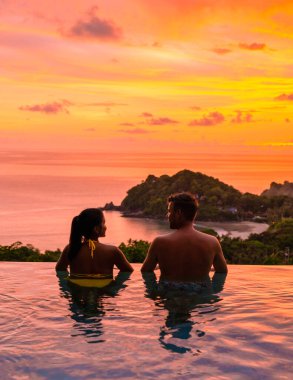 a young couple of men and women at a swimming pool during sunset on a tropical island. man and woman in the infinity pool during sunset. luxury vacation in a luxury pool villa