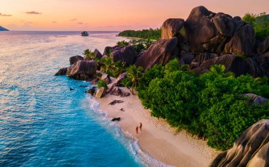 Anse Source dArgent plajı, La Digue Adası, Seyshelles, La Digue Seyşeller 'in insansız hava görüntüsü tropik adanın kuş bakışı görüntüsü, günbatımında sahilde yürüyen iki erkek ve kadın.