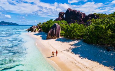 Anse Source dArgent plajı, La Digue Adası, Seyshelles, La Digue Seyşeller 'in insansız hava görüntüsü tropik adanın kuş bakışı görüntüsü, günbatımında sahilde yürüyen iki erkek ve kadın.