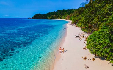 Beyaz tropikal bir plaj ve turkuaz renkli bir okyanusla Koh Kradan Adası sahilinde yürüyen bir çift. Erkekler ve kadınlar yukarıdan Tayland 'da tatil sırasında İHA ile görülmüşler.