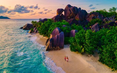 Anse Source dArgent plajı, La Digue Adası, Seyshelles, La Digue Seyşeller 'in insansız hava görüntüsü tropik adanın kuş bakışı görüntüsü, günbatımında sahilde yürüyen iki erkek ve kadın.