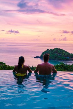 Genç bir çift, tropik bir adada tatil yaparken yüzme havuzunda. Erkek ve kadın gün batımında sonsuz havuzda. Tayland 'da lüks bir havuz villasında lüks bir tatil.