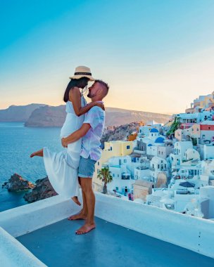 Santorini Yunanistan, Santorini Adası 'nda tatil yapan genç bir çift mavi kubbe kilisesi ve beyazlatılmış Oia Santorini köyü, Asyalı kadınlar ve beyaz tenli erkekler tarafından gün doğumunu izliyor.