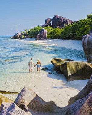 Anse Source dArgent plajı, La Digue Adası, Seyshelles, La Digue Seyşeller 'in insansız hava görüntüsü tropik adanın kuş bakışı görüntüsü, günbatımında sahilde yürüyen iki erkek ve kadın.