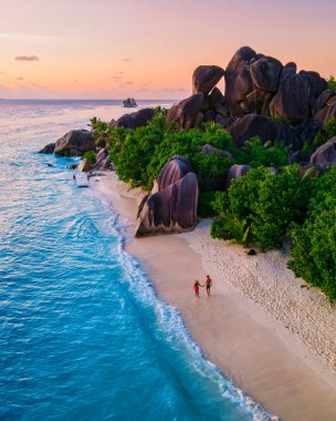 Anse Source dArgent plajı, La Digue Adası, Seyshelles, La Digue Seyşeller 'in insansız hava görüntüsü tropik adanın kuş bakışı görüntüsü, günbatımında sahilde yürüyen iki erkek ve kadın.