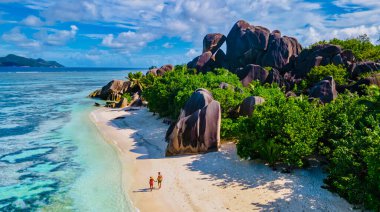 Anse Source dArgent plajı, La Digue Adası, Seyshelles, La Digue Seyşeller 'in insansız hava görüntüsü tropik adanın kuş bakışı görüntüsü, günbatımında sahilde yürüyen iki erkek ve kadın.