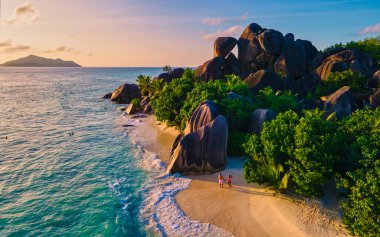Anse Source dArgent plajı, La Digue Adası, Seyshelles, La Digue Seyşeller 'in insansız hava görüntüsü tropik adanın kuş bakışı görüntüsü, günbatımında sahilde yürüyen iki erkek ve kadın.
