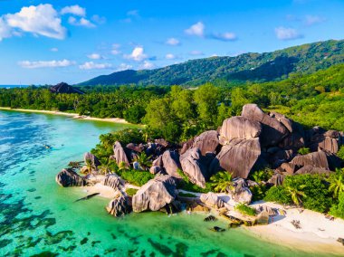 Anse Source dArgent plajı, La Digue Adası, Seyshelles, La Digue Seyşeller 'in insansız hava görüntüsü tropik adanın kuş bakışı görüntüsü, günbatımında sahilde yürüyen iki erkek ve kadın.