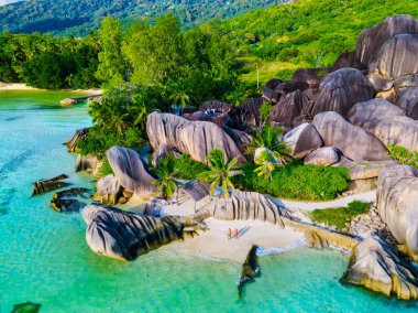 Anse Source dArgent plajı, La Digue Adası, Seyshelles, La Digue Seyşeller 'in insansız hava görüntüsü tropik adanın kuş bakışı görüntüsü, günbatımında sahilde yürüyen iki erkek ve kadın.