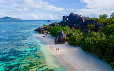Seyşeller 'de lüks bir tatil sırasında, Anse Source dArgent, La Digue Seychelles, tropikal bir plajda genç bir çift kadın ve erkek drone görüntüsü. Tropik sahil Anse Kaynak dArgent, La
