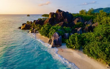 Günbatımı Anse Source dArgent, La Digue Seychelles, Seyşeller 'de lüks bir tatil sırasında tropikal bir plajda iki genç erkek ve kadın. Tropik sahil Anse Kaynak dArgent, La Digue 