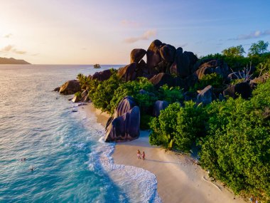 Günbatımı Anse Source dArgent, La Digue Seychelles, Seyşeller 'de lüks bir tatil sırasında tropikal bir plajda iki genç erkek ve kadın. Tropik sahil Anse Kaynak dArgent, La Digue 