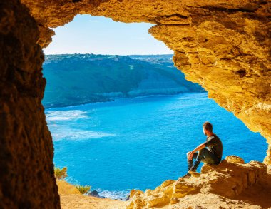 Gozo Adası Malta, genç bir adam ve Ramla Körfezi manzarası, Tal Mixta Mağarası Gozo 'nun içinden açık bir kış günü Malta' da mavi okyanusa bakıyor.
