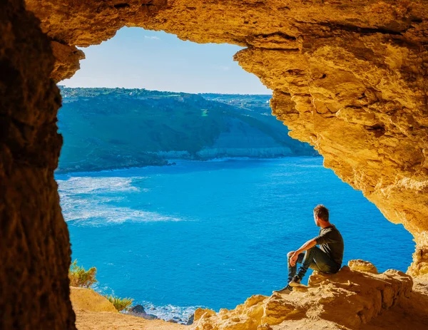 Gozo Adası Malta, genç bir adam ve Ramla Körfezi manzarası, Tal Mixta Mağarası Gozo 'nun içinden açık bir kış günü Malta' da mavi okyanusa bakıyor.