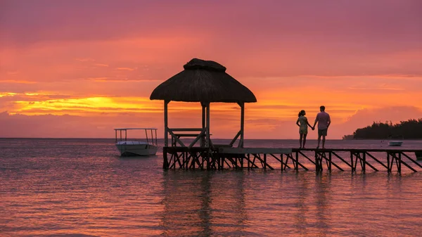 一对男女手牵着手观看落日 在毛里求斯热带海滩上的一个木制码头上 一对夫妇在毛里求斯度蜜月 — 图库照片