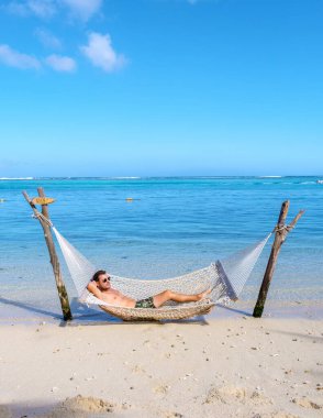 Mauritius 'ta tropikal bir plajda hamakta dinlenen bir adam, güneşli bir günde Mauritius' ta tatilde olan bir adam.