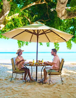 Mauritius 'ta tropik bir plajda kahvaltı yapan erkek ve kadın. Mauritius' ta balayı tatilinde olan bir çift. Ekmek meyvesi ve kahveyle kahvaltı yapan bir çift.