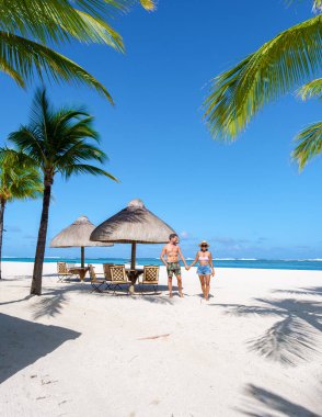 Mauritius 'ta plajda plaj sandalyeleri ve palmiye ağaçları olan bir adam ve kadın. Arka planda Le Morne Dağı ile Mauritius Le Morne Sahili' nde balayı tatili yapan bir çift.