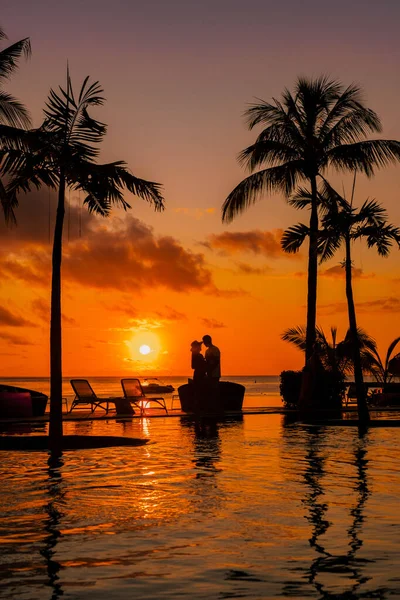a young couple of men and women at a swimming pool during a vacation on a tropical island. man and woman in infinity pool during sunset. luxury vacation in Mauritius pool of a luxury pool villa