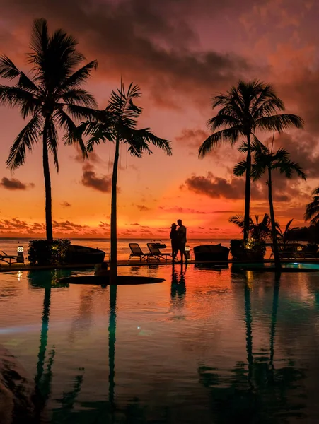 a young couple of men and women at a swimming pool during a vacation on a tropical island. man and woman in infinity pool during sunset. luxury vacation in Mauritius pool of a luxury pool villa