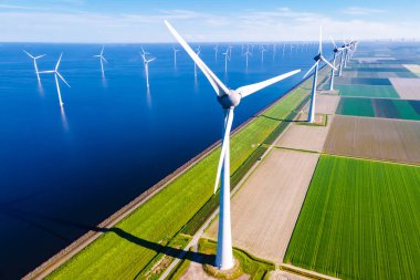 Bulutlu ve mavi gökyüzü olan yel değirmeni parkı okyanustaki yel değirmeni parkı rüzgar türbinleriyle yeşil manzaralı.