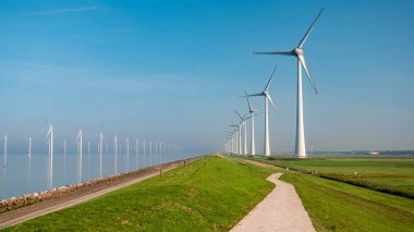 Bulutlu ve mavi gökyüzü olan yel değirmeni parkı okyanustaki yel değirmeni parkı rüzgar türbinleriyle yeşil manzaralı.