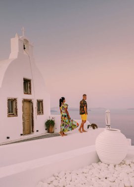 Santorini Yunanistan, Santorini Adası 'nda tatilde olan genç bir çift, yaz tatilinde güneş doğarken mavi kubbe kilisesi ve beyazlatılmış Oia Santorini köyünün doğuşunu izliyor.