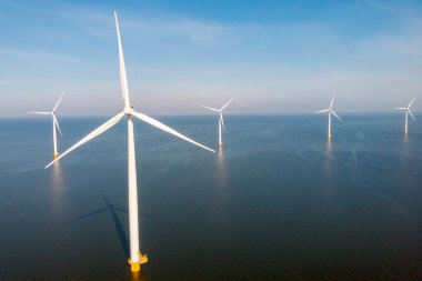 Bulutları ve mavi gökyüzü olan rüzgar değirmeni parkı, okyanusta yel değirmeni türbinleri