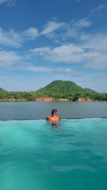タイの休暇のプールの端にある男性は セントラルタイの湖と緑の山を眺めています — ストック動画