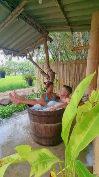 タイ中部のグリーンライス田畑と竹小屋ホームステイ農場の木製浴槽に男女2人 — ストック動画