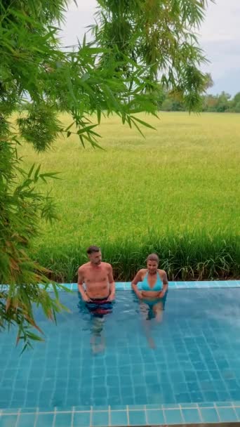 バンブー小屋ホームステイ農場の前にいる男女のカップルと 小さなプランジプールがある中央タイのグリーンライス田畑 — ストック動画