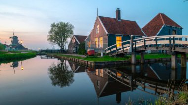 Hollanda 'da bahar aylarında gün batımında yel değirmeni köyü Zaanse Schans' ta günbatımında tarihi ahşap çiftlikleri olan tarihi Hollanda köyünde.