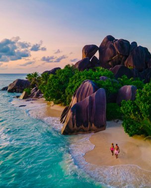 Anse Source dArgent plajı, La Digue Adası, Seyshelles, La Digue Seyşeller 'in insansız hava görüntüsü tropik adanın kuş bakışı görüntüsü, günbatımında sahilde yürüyen iki erkek ve kadın.